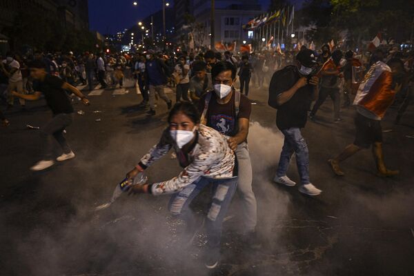 Susținătorii fostului președinte Pedro Castillo se acoperă de gazele lacrimogene aruncate de poliție în timpul ciocnirilor de la o demonstrație care cere eliberarea lui și închiderea Congresului peruan de la Lima, 11 decembrie 2022 - Sputnik Moldova
