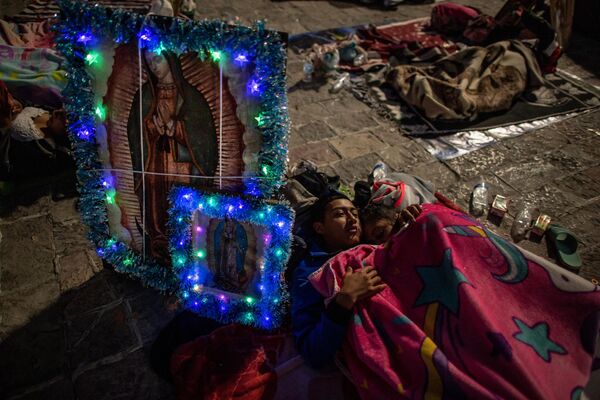 Пара отдыхает рядом с изображениями Девы Гваделупской в ​​лагере с другими паломниками в ​​Мехико. - Sputnik Молдова