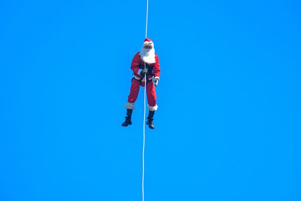 Муниципальный пожарный Гектор Чакон в костюме Санта-Клауса спускается по канату с моста, чтобы доставить подарки детям в Гватемале. - Sputnik Молдова