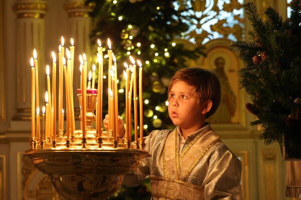 Мальчик зажигает свечу во время празднования православного Рождества в Русской православной церкви в Шардже. - Sputnik Молдова