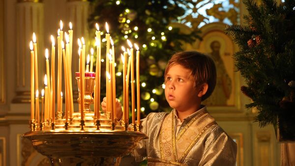 Мальчик зажигает свечу во время празднования православного Рождества в Русской православной церкви в Шардже - Sputnik Молдова