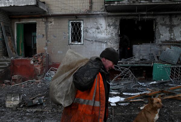 Мужчина выносит мусор с территории дома, пострадавшего в результате ночного обстрела в Горловке - Sputnik Молдова