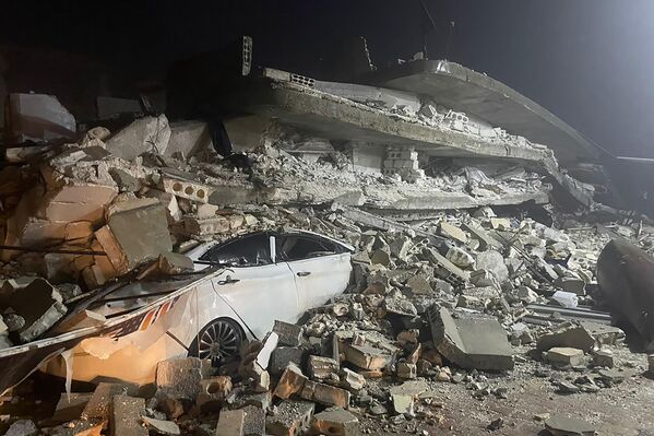 O mașină este văzută sub epava unei clădiri prăbușite, în orașul Azmarin din provincia Idlib, nordul Siriei, 6 februarie 2023 - Sputnik Moldova-România