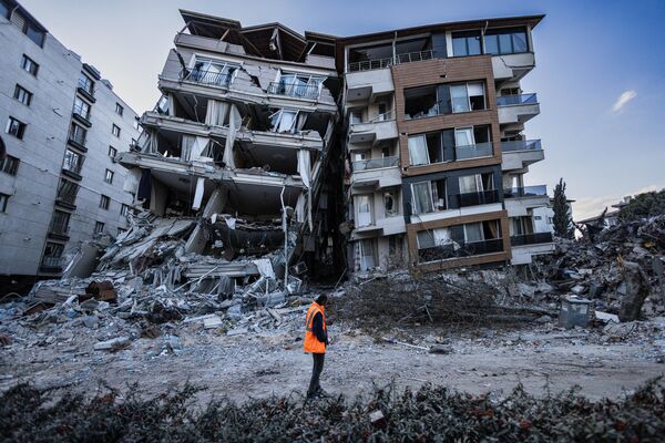 Спасатель проходит мимо частично разрушенных в результате землетрясений зданий в городе Антакья, Турция - Sputnik Молдова