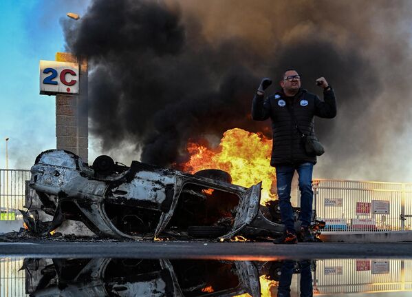 Член профсоюза Всеобщей конфедерации труда стоит рядом с перевернутой горящей машиной во время блокады марсельского порта во Франции. - Sputnik Молдова