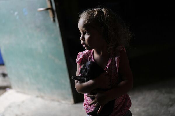 Девочка несет щенка, пока ее бабушка наполняет емкость водой из колодца в районе Петаре в Каракасе. - Sputnik Молдова