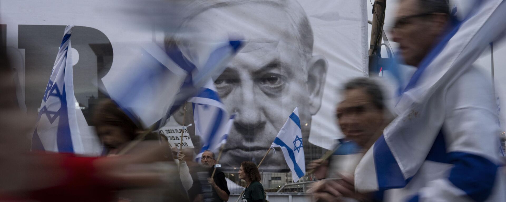 Демонстранты с  флагами Израиля рядом с баннером с изображением премьер-министра Биньямина Нетаньяху во время акции  против реформы судебной системы в Тель-Авиве, Израиль - Sputnik Молдова, 1920, 28.03.2023