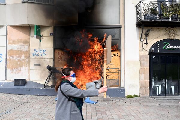 O persoană trece pe lângă  intrarea în sucursala băncii Paribas, care este cuprinsă de flăcări, în timpul unei demonstrații de protest la Nantes în vestul Franței. 28 martie 2023 - Sputnik Moldova-România