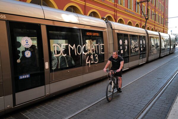 Un bărbat trece cu bicicleta pe lângă un un vagon de tramvai, unde este inscripționat cuvântul: „Decocrația 49.3”, în timp ce au loc demonstrații de masă  în Franța - Sputnik Moldova-România