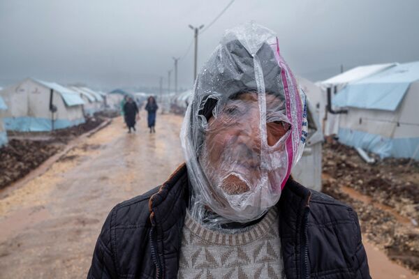 Турецкий мужчина с полиэтиленовым пакетом от дождя на голове у палаток, установленных для вынужденных переселенцев после сильного землетрясения, произошедшего в феврале в Адыямане, Турция. - Sputnik Молдова