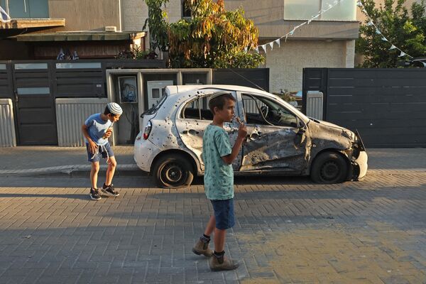 Дети смотрят на поврежденный автомобиль в южном израильском городе Сдерот 2 мая 2023 года после столкновения между израильскими военными и боевиками Газы. - Sputnik Молдова