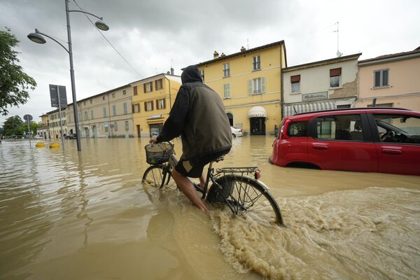 Велосипедист едет по затопленной улице в деревне Кастель-Болоньезе,  региона Эмилия-Романья, Италия. - Sputnik Молдова