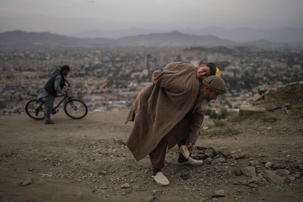 61-летний Абдул Кадер Газизада убирает камни с дороги, неся своего 2-летнего сына Ахмада Сира, чтобы велосипеды и автомобили лучше передвигались по району Tape TV в Кабуле, Афганистан, воскресенье, 28 мая 2023 года. - Sputnik Молдова