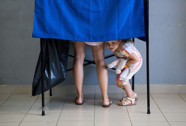 Девочка смотрит из кабины для голосования на избирательном участке во время всеобщих выборов в Афинах, Греция. - Sputnik Молдова
