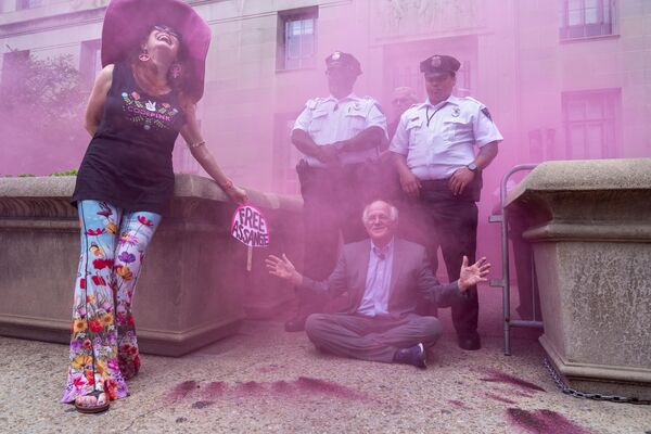 Jodie Evans, stânga, co-fondatorul grupului de protest CODEPINK, reacționează în timp ce Ben Cohen, co-fondatorul Ben &amp; Jerry&#x27;s, face gesturi prin curățarea fumului roz în timpul unui protest în timp ce blochează intrarea în Departamentul de Justiție, în timpul unui protest impotriva acuzării fondatorului Wikileaks, Julian Assange, joi, 6 iulie 2023, în fața Departamentului de Justiție din Washington. (AP Foto/Jacquelyn Martin) - Sputnik Moldova