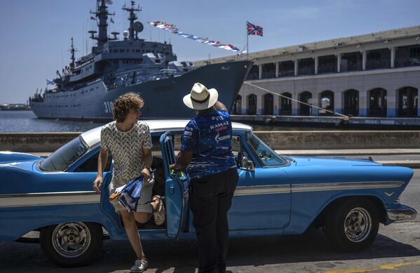 Un turist coboară dintr-o mașină americană clasică în fața navei de antrenament a Marinei ruse Perekop din Golful Havana, Cuba - Sputnik Moldova