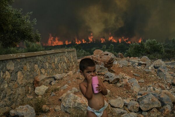 Ребенок во дворе своего дома на фоне лесного пожара в деревне Агиос Харалампос, недалеко от Афин, Греция. - Sputnik Молдова