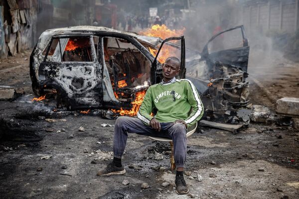 Сторонник кенийской оппозиции позирует на фоне подожженного протестующими автомобиля во время беспорядков в Найроби. - Sputnik Молдова