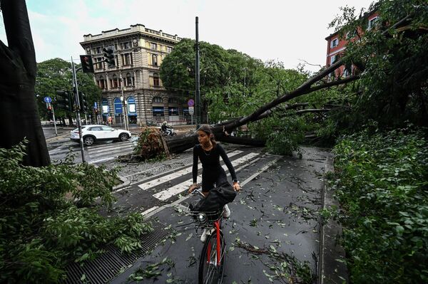 Местная жительница едет на велосипеде через упавшие деревья в центре Милана 25 июля 2023 года после ночного ливня, обрушившегося на город. - Sputnik Молдова