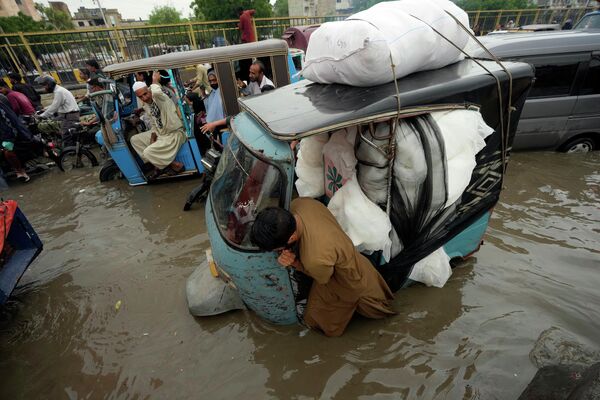 Водитель толкает свою рикшу по затопленной дороге, вызванной сильными муссонными дождями, в Карачи, Пакистан, понедельник, 24 июля 2023 года.  - Sputnik Молдова