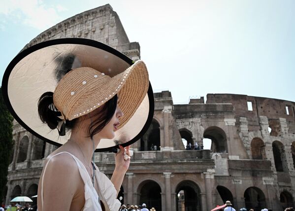 Туристка укрывается от солнца панелью, проходя мимо Колизея в Риме, 24 июля 2023 года, во время сильной жары в Италии. - Sputnik Молдова