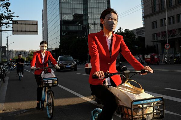 Женщины в масках едут на велосипедах по улице в Пекине 25 июля 2023 года. - Sputnik Молдова