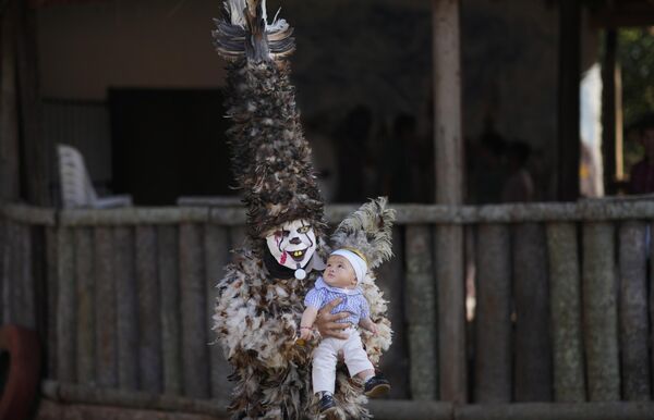 Человек в маске, одетый в костюм с перьями, держит ребенка на руках, позируя для портрета перед мессой в честь святого Франциско в Эмбоскаде, Парагвай, понедельник, 24 июля 2023 года.  - Sputnik Молдова