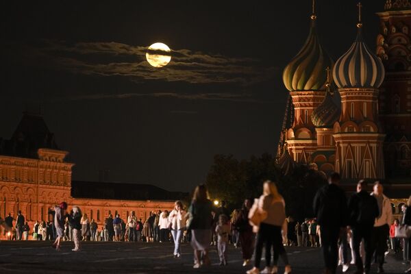 Super Luna Albastră din august se așterne în spatele unei clădiri istorice și al Catedralei Sf. Vasile, în dreapta, în timp ce oamenii merg în Piața Roșie din Moscova. - Sputnik Moldova