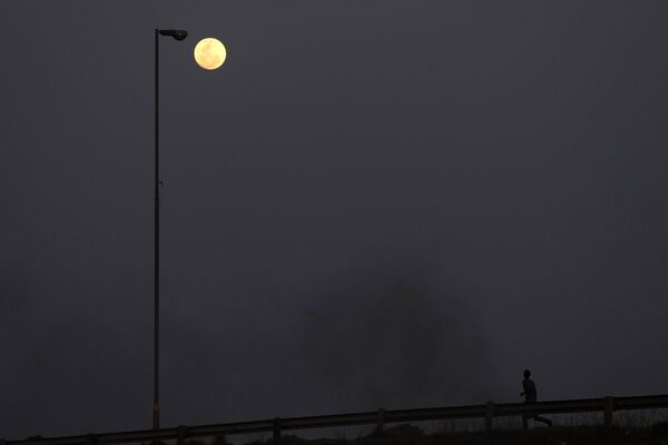 O Superlună este văzută pe cer în timp ce un bărbat aleargă pe o stradă din Vosloorus, oraș situat la est de Johannesburg, Africa de Sud, 30 august 2023. - Sputnik Moldova