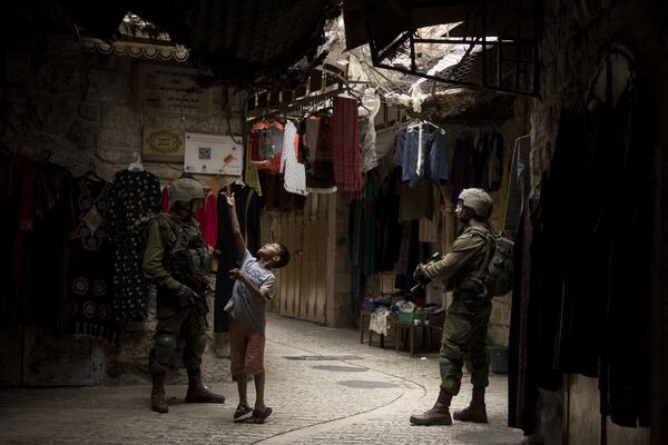 Палестинский мальчик и израильские солдаты на рынке в городе Хеврон на Западном Берегу во время Суккота, недельного праздника в ознаменование 40-летия странствий израильтян по пустыне. - Sputnik Молдова