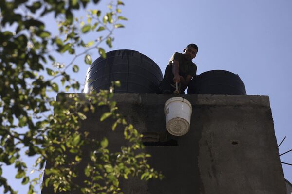 Мужчина поднимает ведро с водой на крышу, чтобы наполнить резервуар для воды в доме в лагере беженцев Рафах, на юге сектора Газа. - Sputnik Молдова