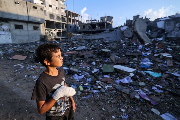 Раненый палестинский мальчик смотрит на здания, разрушенные во время израильских авиаударов, недалеко от его дома в лагере беженцев Рафах на юге сектора Газа. - Sputnik Молдова