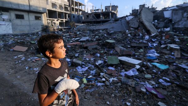 Раненый палестинский мальчик смотрит на здания, разрушенные во время израильских авиаударов, недалеко от его дома в лагере беженцев Рафах на юге сектора Газа - Sputnik Moldova