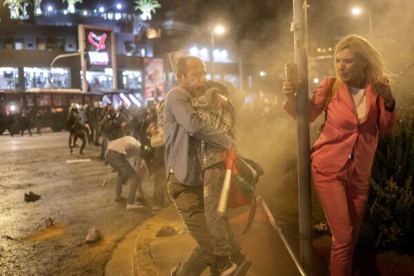 Мужчина держит мальчика, пока протестующие бегут от слезоточивого газа, выпущенного полицией по охране общественного порядка во время митинга в поддержку палестинцев, возле посольства Израиля в Афинах 18 октября 2023 года. - Sputnik Молдова