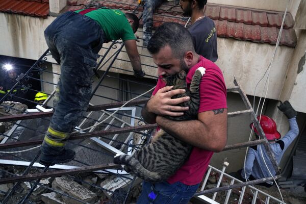 Мужчина обнимает кошку после того, как ее вытащили живой из-под обломков частично обрушившегося здания в ливанском городе Мансури, к юго-востоку от Бейрута, Ливан, понедельник, 16 октября 2023 года. - Sputnik Молдова