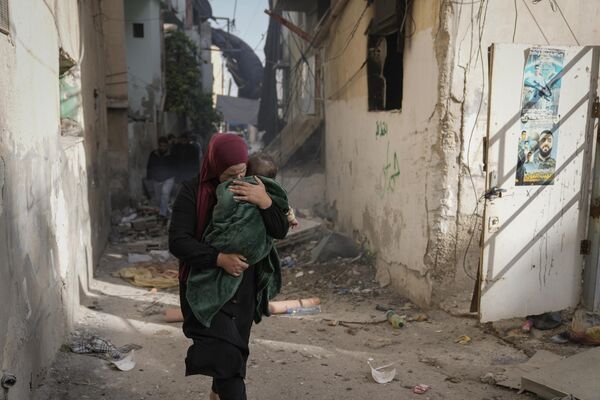 Женщина с ребенком проходит мимо поврежденного здания после операции израильской армии в лагере беженцев Дженин - Sputnik Молдова