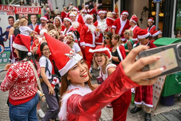 Женщина в костюме Санта-Клауса делает селфи во время ежегодного фестиваля SantaCon в Гонконге 9 декабря 2023 года. - Sputnik Молдова