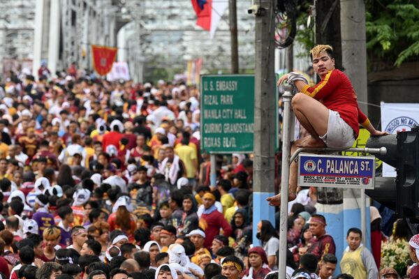 Католик сидит на дорожном знаке во время ежегодного религиозного шествия, проводимого в честь так называемого &quot;Черного назарянина&quot; в Маниле. - Sputnik Молдова