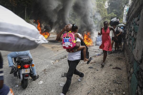 Люди проходят мимо горящих шин во время акции протеста против премьер-министра Гаити Ариэля Генри в Порт-о-Пренсе, Гаити. - Sputnik Молдова
