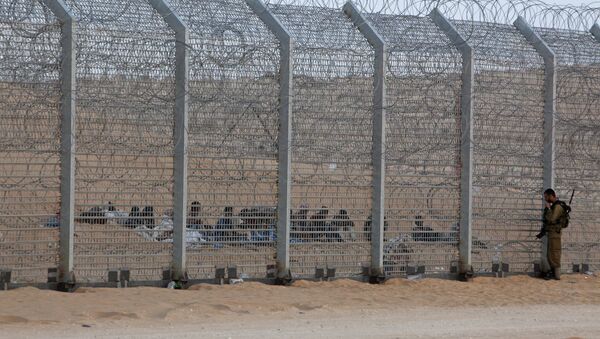 An Israeli soldier stands near the border fence between Israel and Egypt as African would-be immigrants sit on the other side near the Israeli village of Be'er Milcha, in this September 6, 2012 file photo - Sputnik Moldova-România
