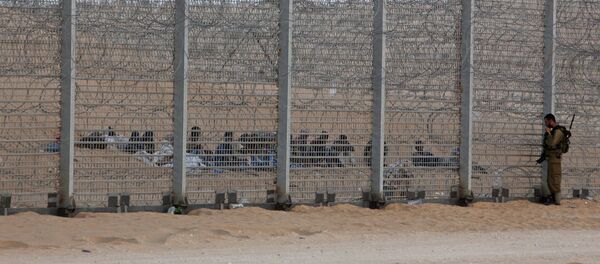 An Israeli soldier stands near the border fence between Israel and Egypt as African would-be immigrants sit on the other side near the Israeli village of Be'er Milcha, in this September 6, 2012 file photo - Sputnik Moldova-România