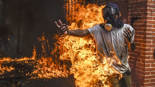 Демонстрант, охваченный огнем от взрыва бензобака мотоцикла, во время протестов в Венесуэле - Sputnik Молдова