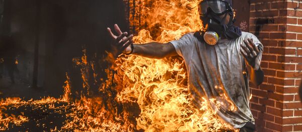 Демонстрант, охваченный огнем от взрыва бензобака мотоцикла, во время протестов в Венесуэле - Sputnik Молдова