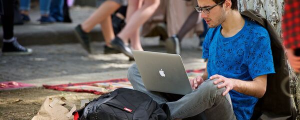 Молодой человек работает за ноутбуком, сидя на земле в парке. Хипстерский рынок - Sputnik Молдова