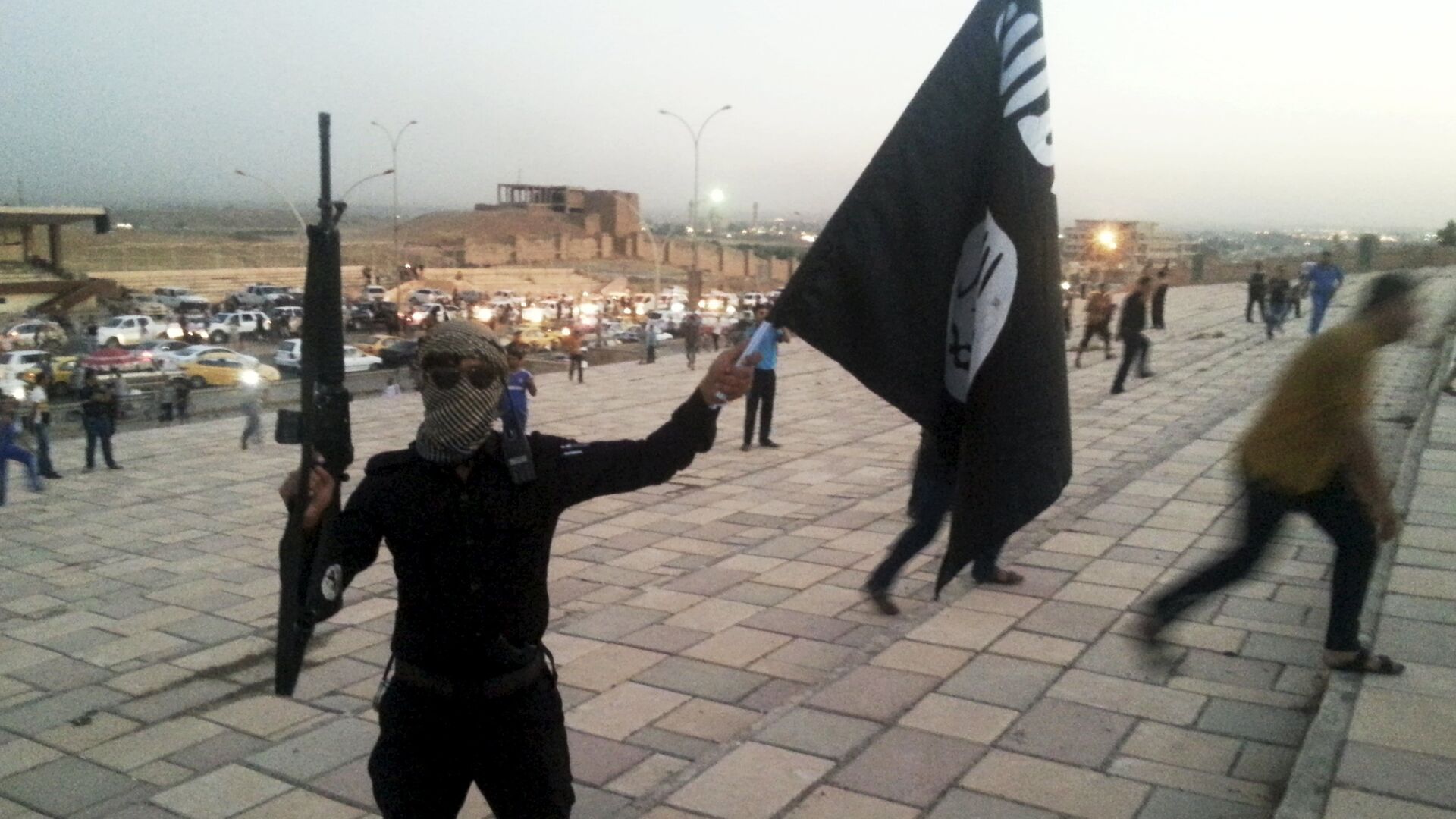 A fighter of Daesh holds an ISIL flag and a weapon on a street in the city of Mosul, Iraq, in this June 23, 2014. - Sputnik Moldova-România, 1920, 27.10.2021