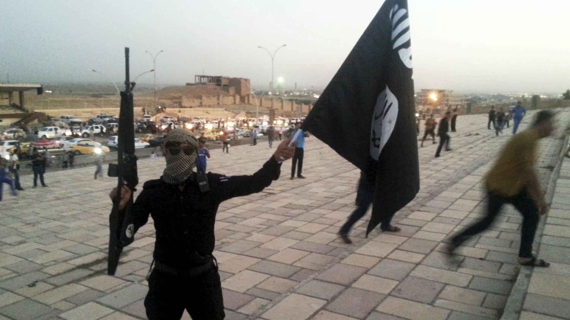 A fighter of Daesh holds an ISIL flag and a weapon on a street in the city of Mosul, Iraq, in this June 23, 2014. - Sputnik Moldova-România, 1920, 06.05.2021