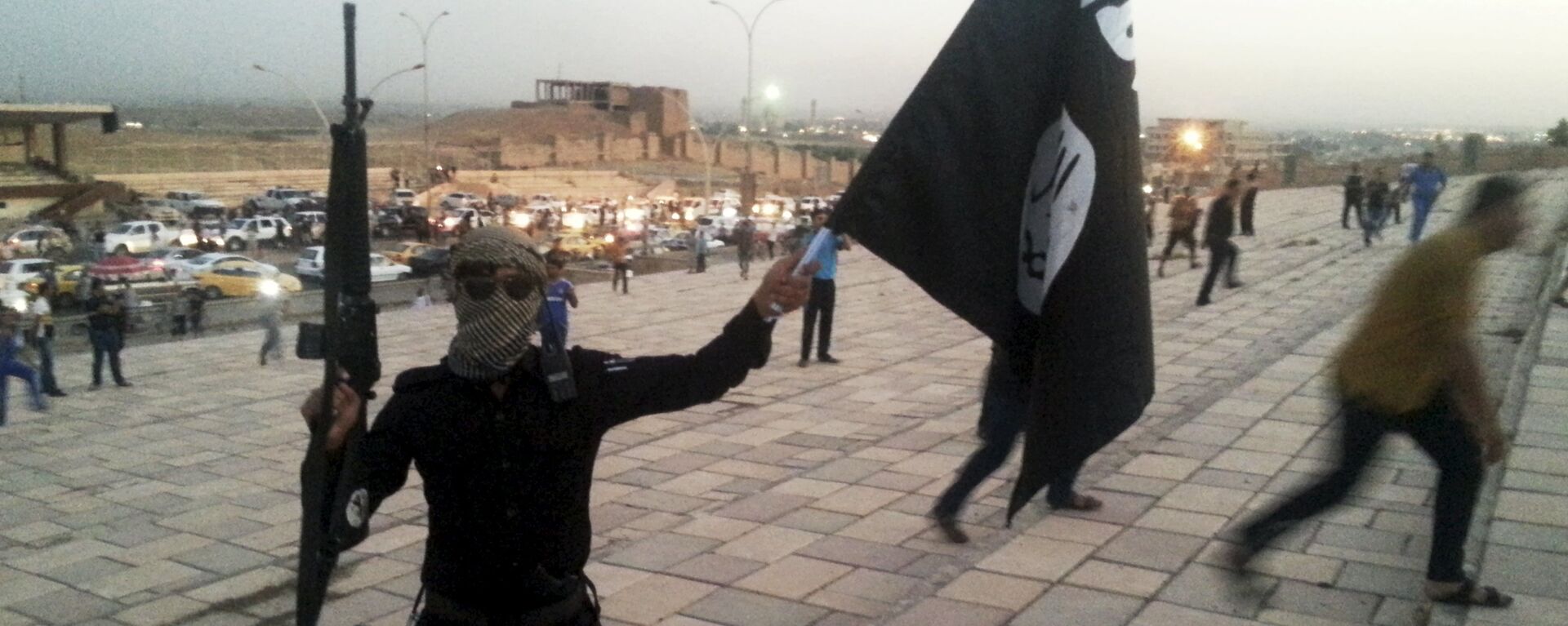 A fighter of Daesh holds an ISIL flag and a weapon on a street in the city of Mosul, Iraq, in this June 23, 2014. - Sputnik Moldova-România, 1920, 19.05.2020