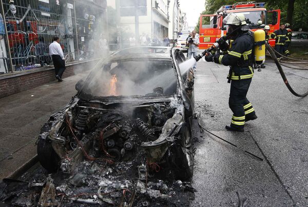 Пожарный тушит машину, сожженную в ходе акций протеста в Гамбурге против саммита G20 - Sputnik Молдова