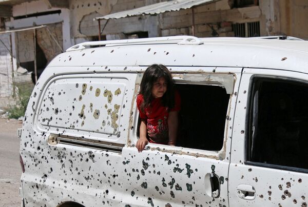 Девочка смотрит из разбитого окна автобуса, весь кузов которого изрешечен пулями, в Сирии - Sputnik Молдова