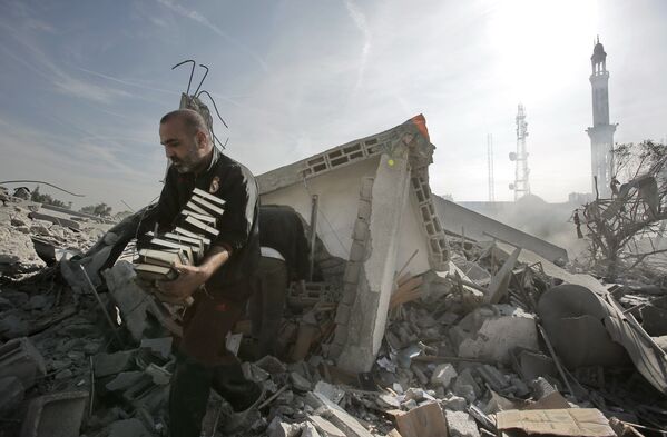 Мужчина выносит стопки Корана из разрушенного взрывом здания в Газе, 2012 год - Sputnik Молдова